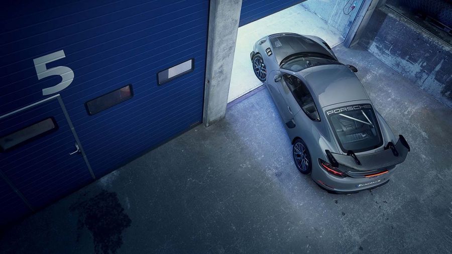Porsche 718 GT4 RS in lila Metallic-Lackierung, von oben fotografiert, fährt in eine moderne Garage ein.